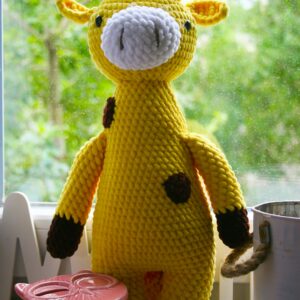 Bright yellow knitted giraffe toy on window sill with greenery outside, perfect for cozy interiors.