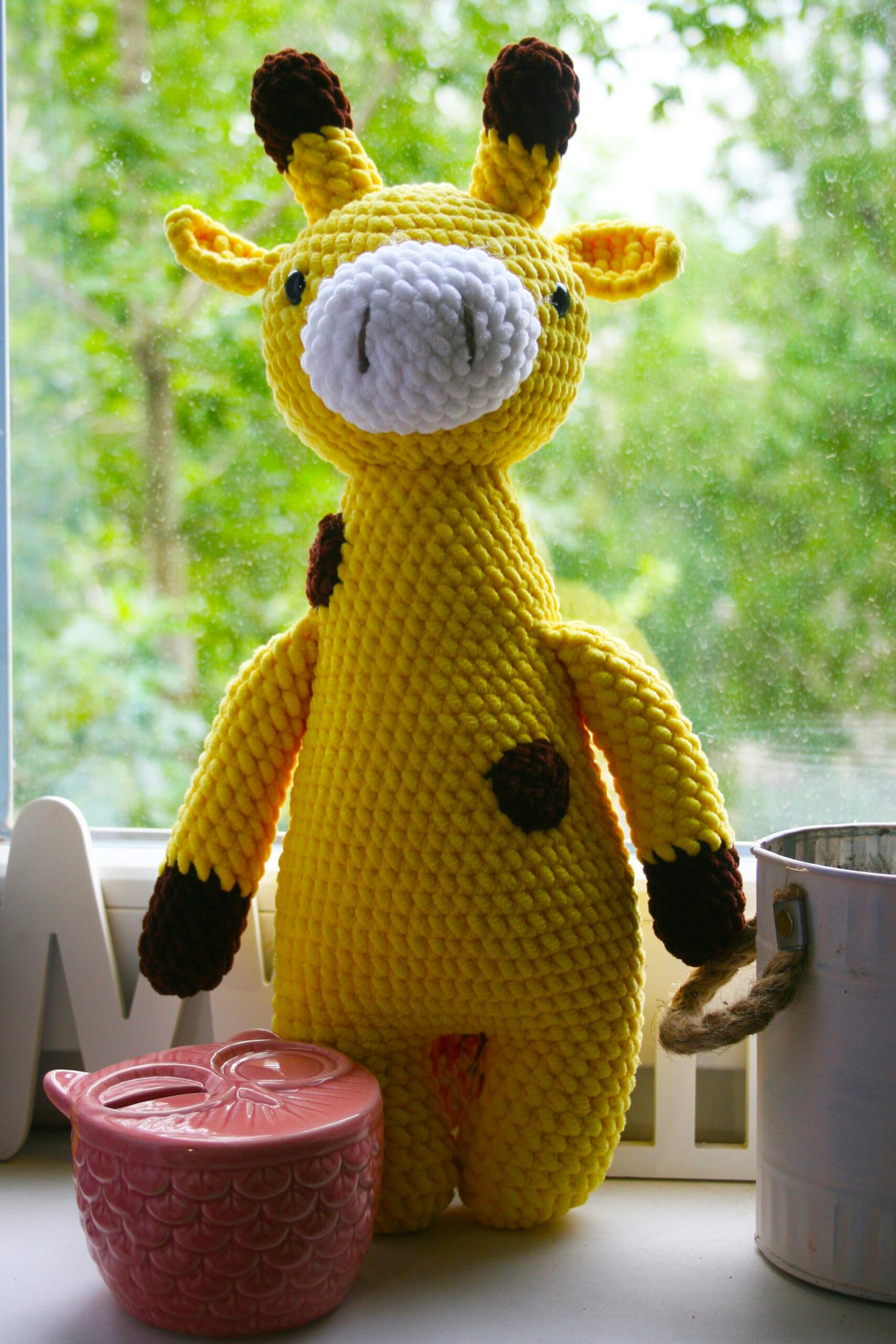 Bright yellow knitted giraffe toy on window sill with greenery outside, perfect for cozy interiors.