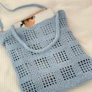 A stylish handmade blue knit bag holding a magazine on a soft textile background.
